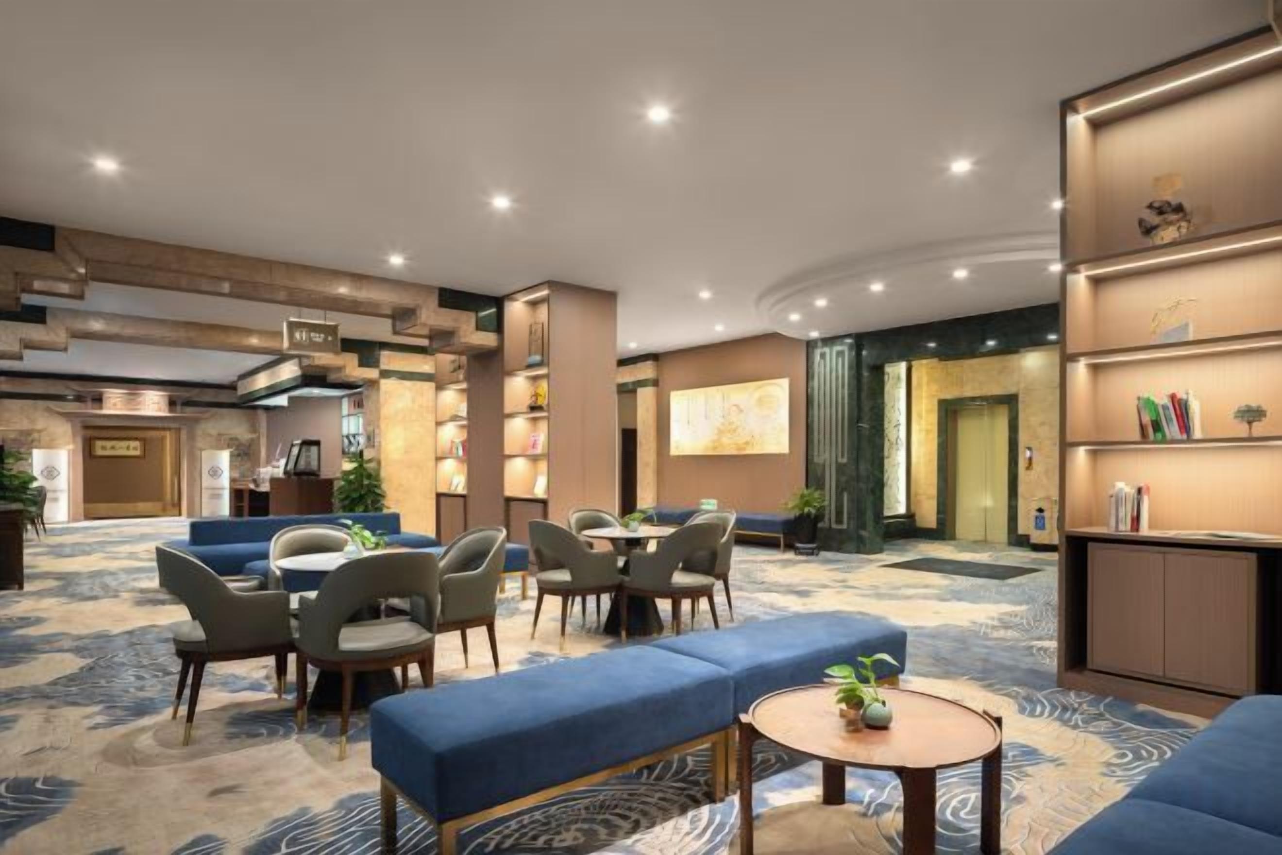 Un vestíbulo de hotel con zonas de estar, mostrador de recepción y una estantería.