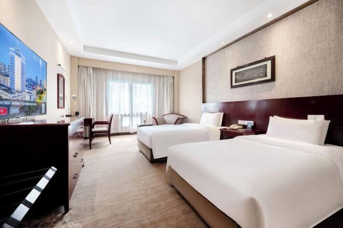 A hotel room with two beds, a desk, a chair, and a TV.