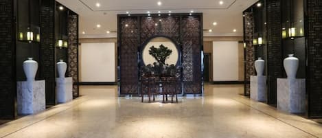 A spacious lobby with a marble floor, a central seating area with a table and chairs, and decorative vases on either side.