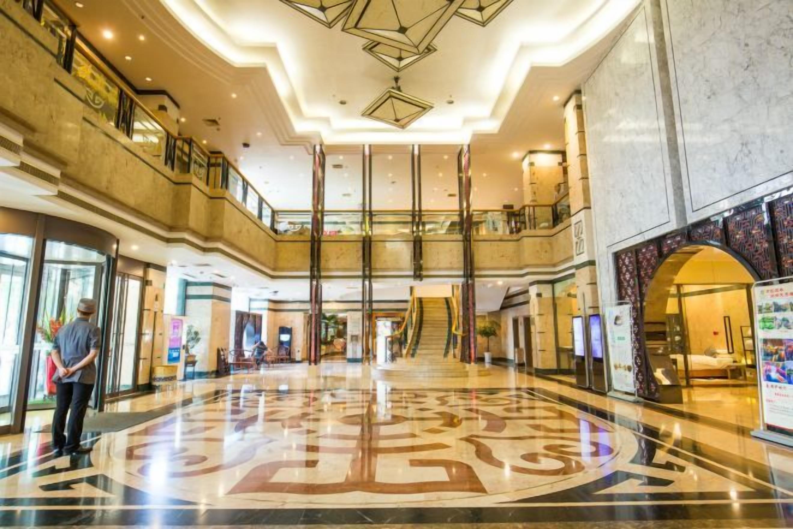 A spacious lobby with a high ceiling, a central staircase, and a polished marble floor.