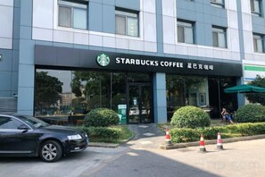 Un café Starbucks à l’architecture moderne, une voiture garée devant, et un piéton qui passe.