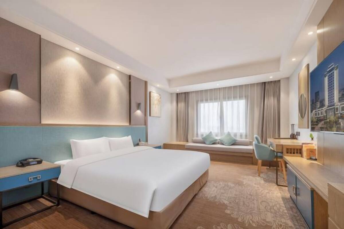 A modern hotel room with a large bed, a desk, and a seating area with a view of the city.
