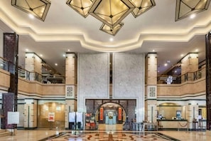 A spacious lobby with a central reception desk, multiple floors, and a modern chandelier design.