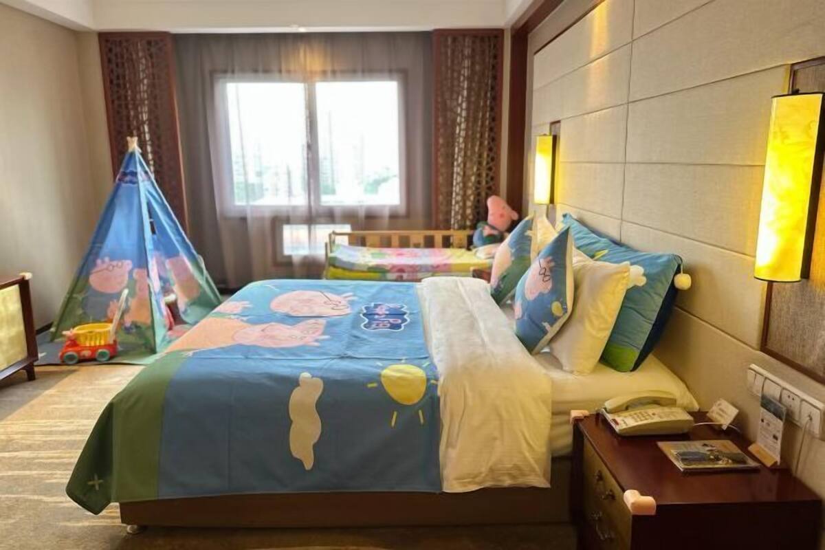 A hotel room with a bed, a desk, a lamp, and a window.