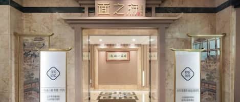 Entrada de hotel com um letreiro sobre a porta, balcão de recepção e duas colunas com logotipos.