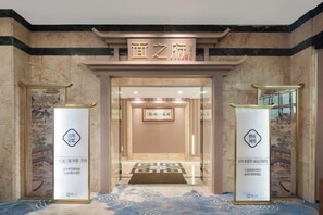 Entrada de hotel con un letrero sobre la puerta, un mostrador de recepción y dos pilares con logotipos.
