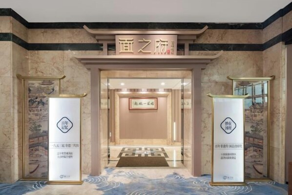 Entrada de hotel con un letrero sobre la puerta, un mostrador de recepción y dos pilares con logotipos.