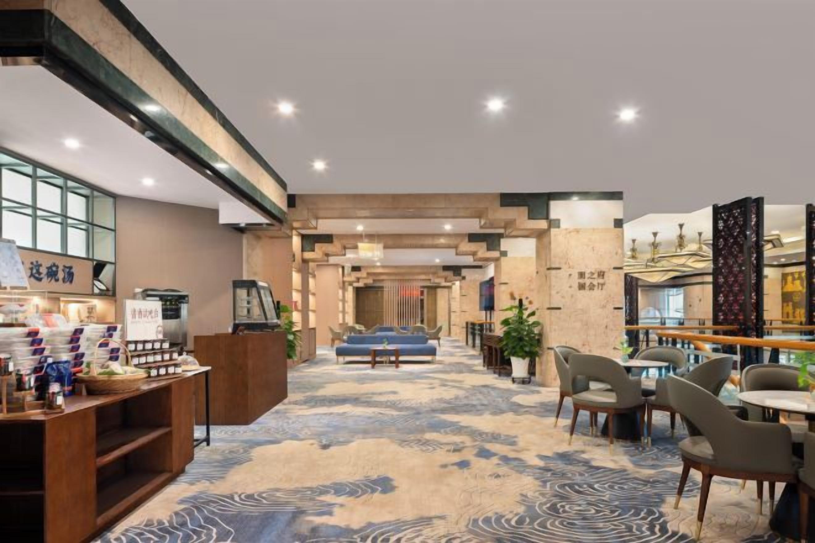 Um hall de hotel com balcão de recepção, área de estar e carpete estampado.