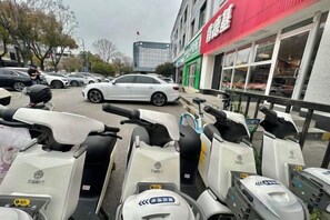 Une rangée de scooters est stationnée devant un immeuble surmonté d’un auvent rouge.