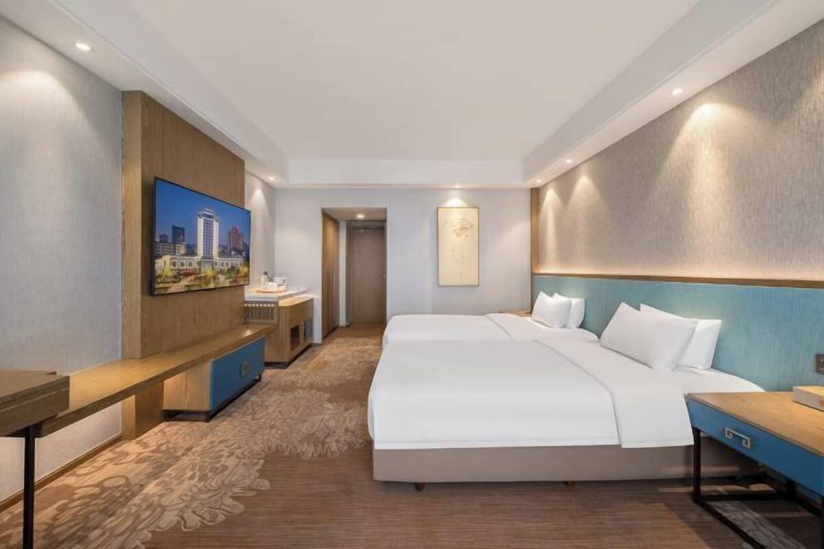 A hotel room with a large bed, a desk, a chair, a TV, and a painting on the wall.