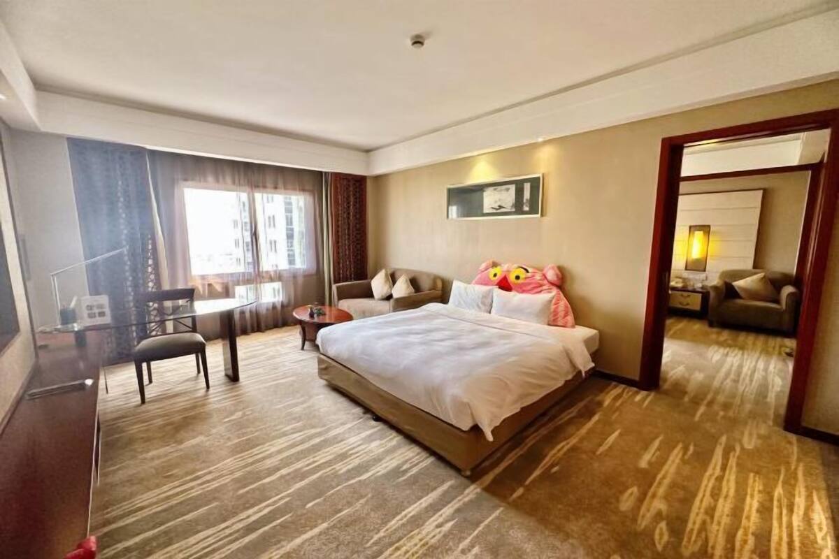 A hotel room with a bed, a desk, a chair, a small table, and a mirror.