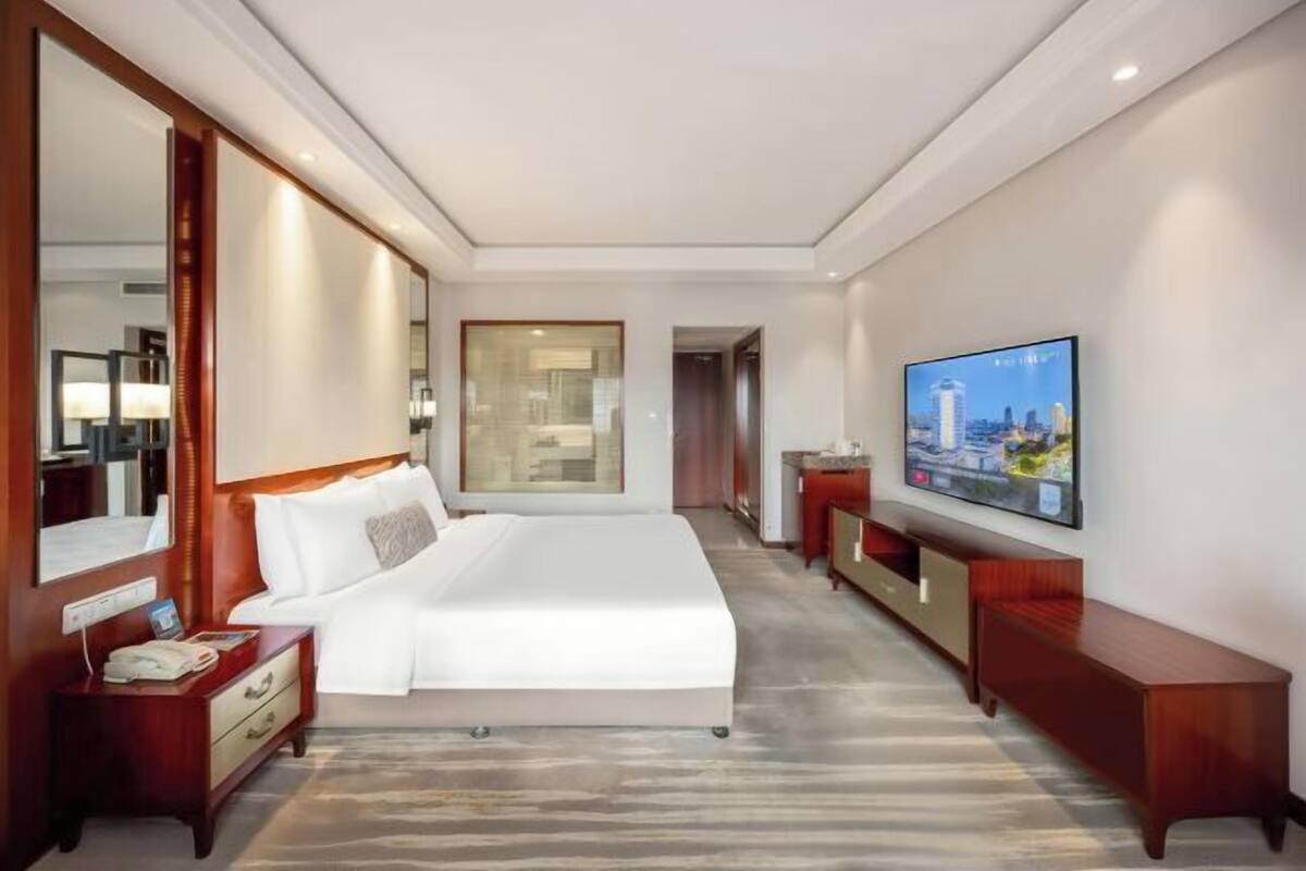A hotel room with a large bed, a TV, a mirror, and a wooden nightstand.
