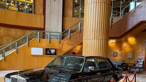 A black Rolls Royce on display with a red rope barrier, surrounded by a polished marble floor and a staircase in the background. - Shantou Junhua Haiyi Hotel (Shantou)