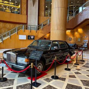 A black Rolls Royce on display with a red rope barrier, surrounded by a polished marble floor and a staircase in the background. - Shantou Junhua Haiyi Hotel (Shantou)