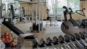 A gym with various exercise equipment, a bench, dumbbells, and a TV screen. - Shantou Junhua Haiyi Hotel (Shantou)