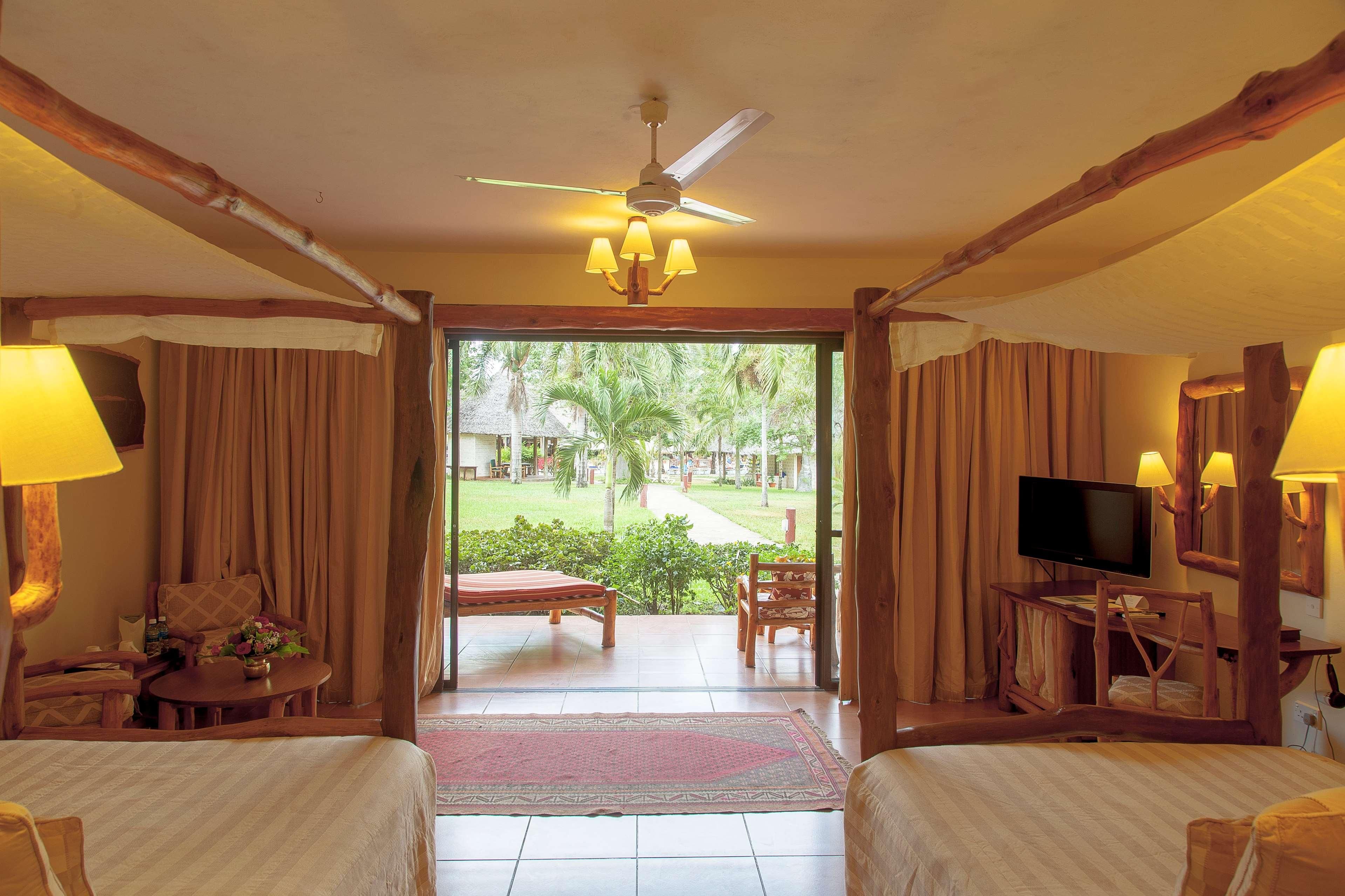 Habitación de hotel con cama, televisor, escritorio y vista a un jardín.