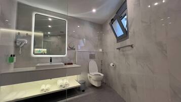 A modern bathroom with a large mirror, a built-in hairdryer, a toilet, and a shelf with towels.