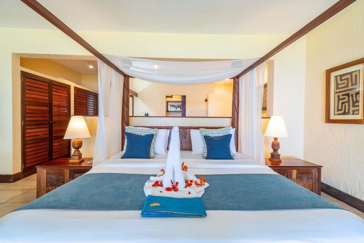 A hotel room with a large bed, two nightstands, a canopy over the bed, and a view of the hallway.