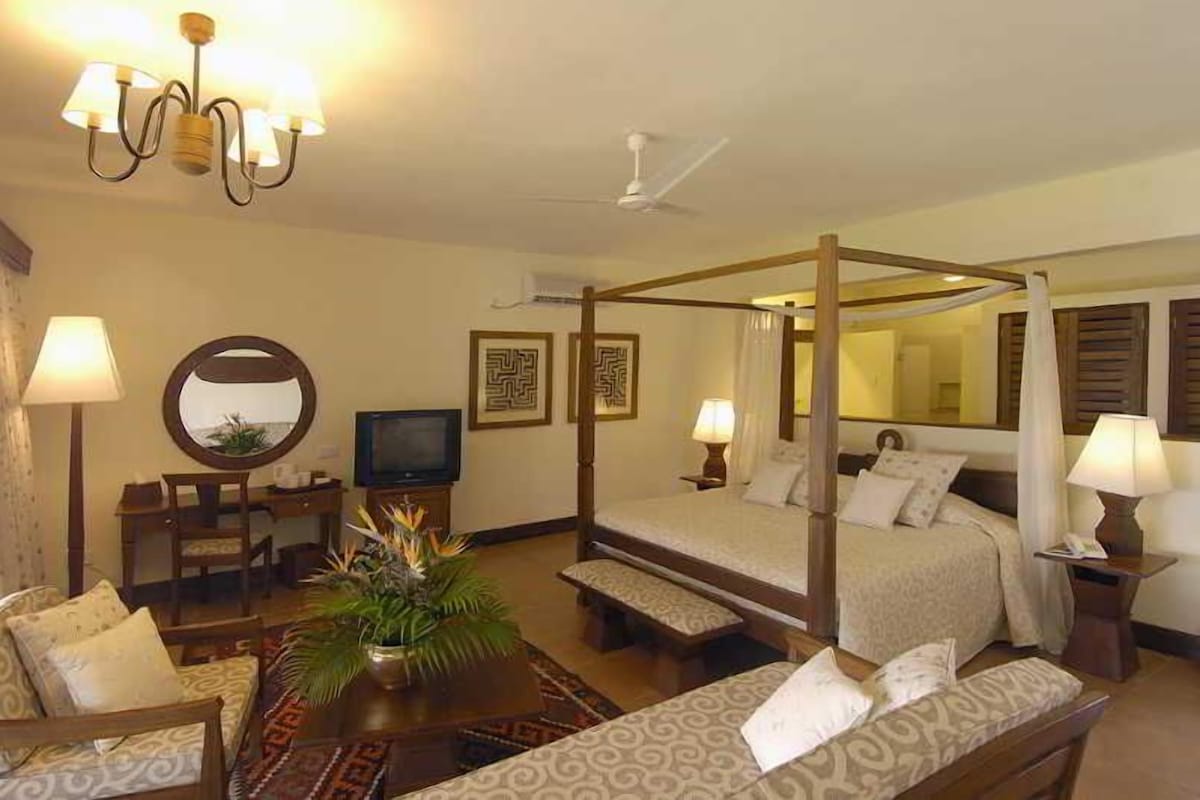 A four-poster bed with a canopy, a television, a desk with a chair, and a sofa.