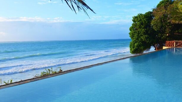 A clear view of a swimming pool with a view of the ocean and a tree-lined area. - Baobab Beach Resort (Diani Beach)