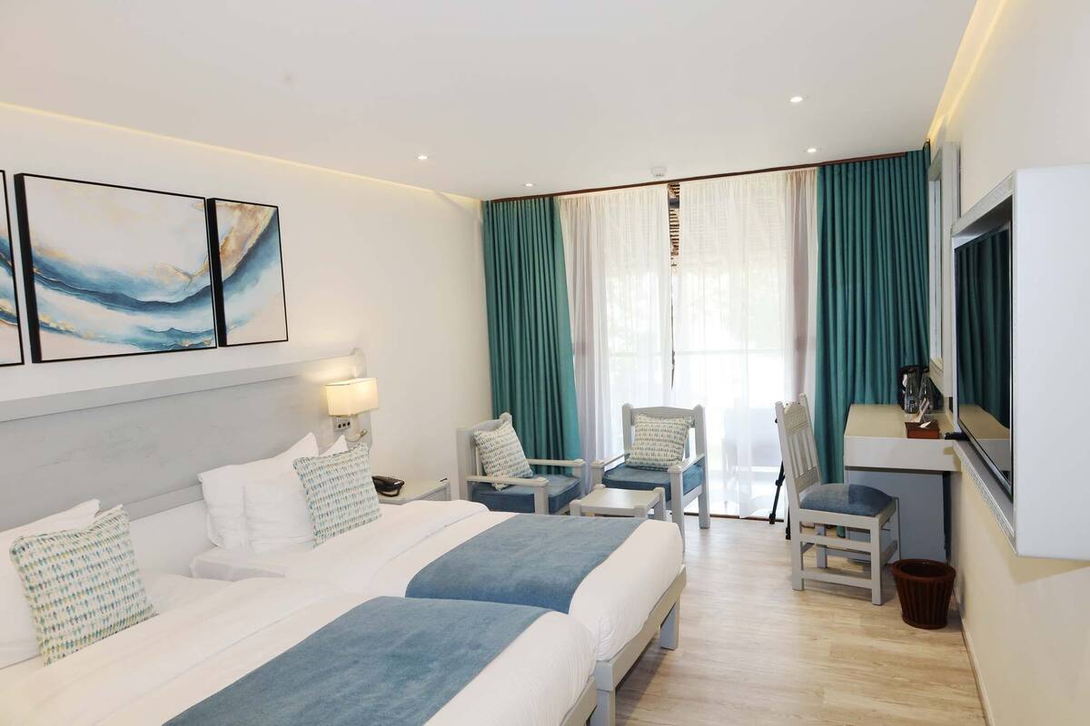 A hotel room with two beds, a desk, a chair, a TV, and a window with curtains.