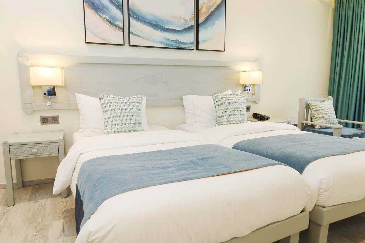 A hotel room with two beds, a nightstand, a chair, and a wall-mounted phone.