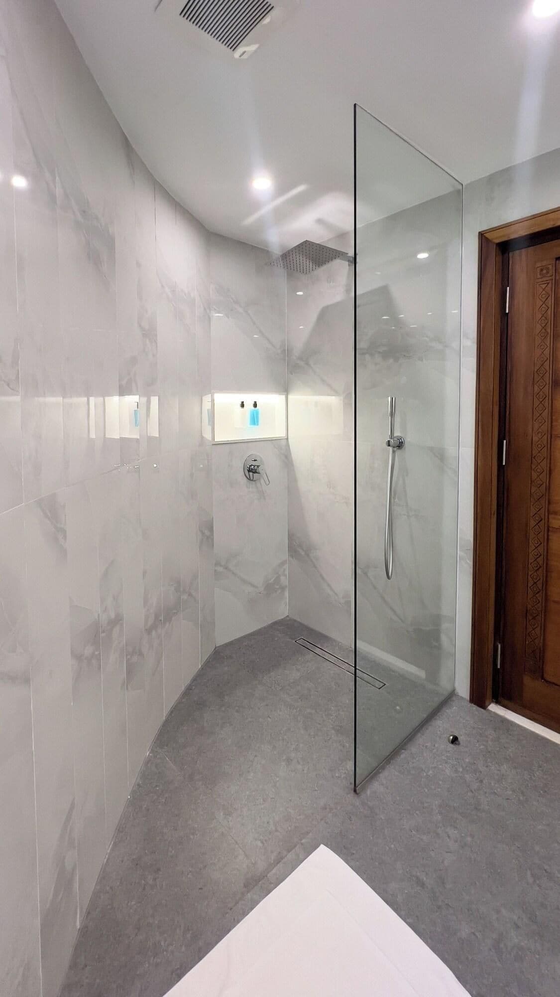 A modern bathroom with a glass shower enclosure, marble walls, and a wooden door.