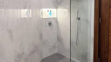 A modern bathroom with a glass shower enclosure, marble walls, and a wooden door.