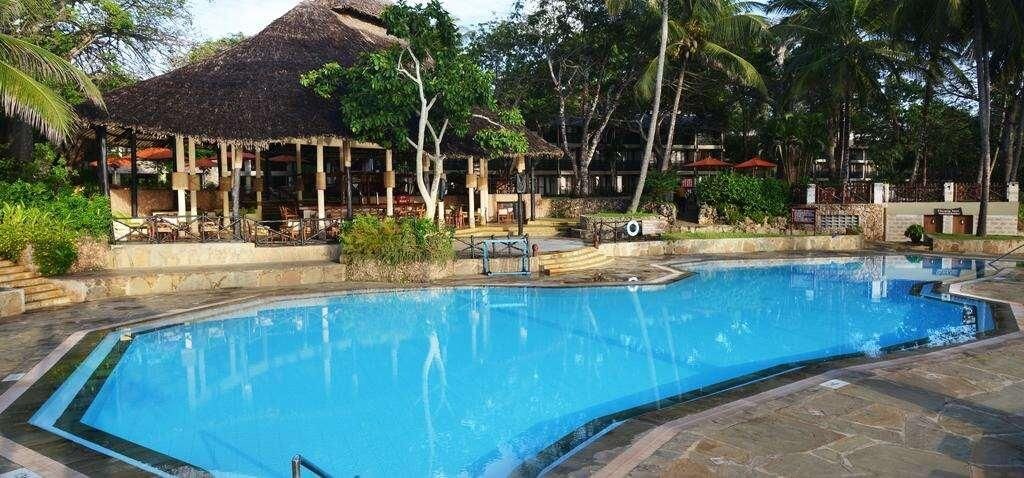 A swimming pool with a thatched-roof structure and lounge chairs in the background.