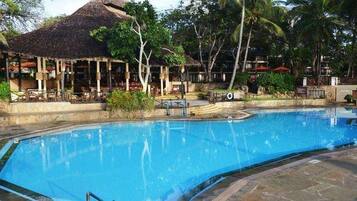 A swimming pool with a thatched-roof structure and lounge chairs in the background.