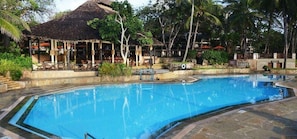 A swimming pool with a thatched-roof structure and lounge chairs in the background. - Baobab Beach Resort (Diani Beach)