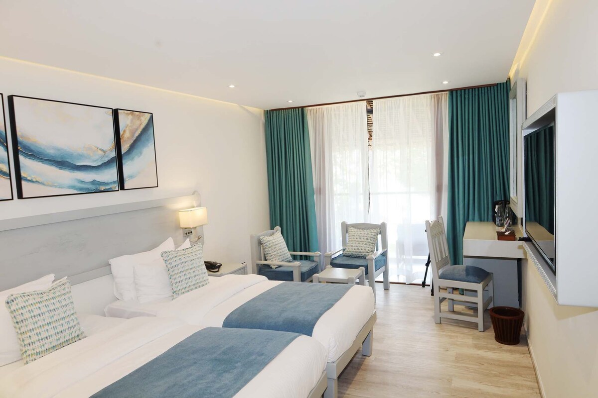 A hotel room with two beds, a desk, a chair, a TV, and a window with curtains.