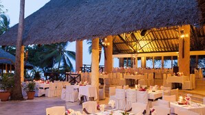 A restaurant with white tablecloths, candle-lit centerpieces, and a thatched roof structure. - Baobab Beach Resort (Diani Beach)
