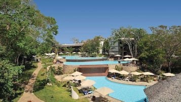 Un resort con varias piscinas, zonas de descanso y un camino que atraviesa un jardín ajardinado.