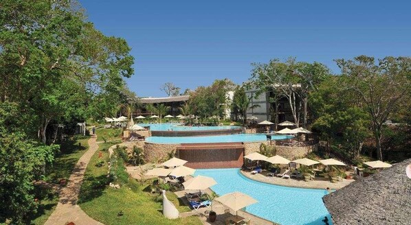 Un resort con varias piscinas, zonas de descanso y un camino que atraviesa un jardín ajardinado.