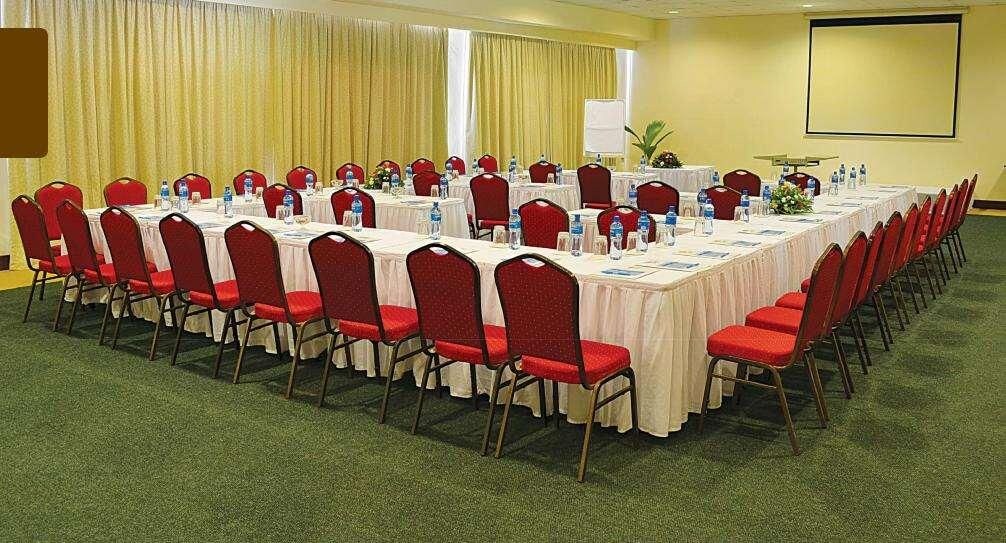 A conference room with long tables, red chairs, and a projector screen.