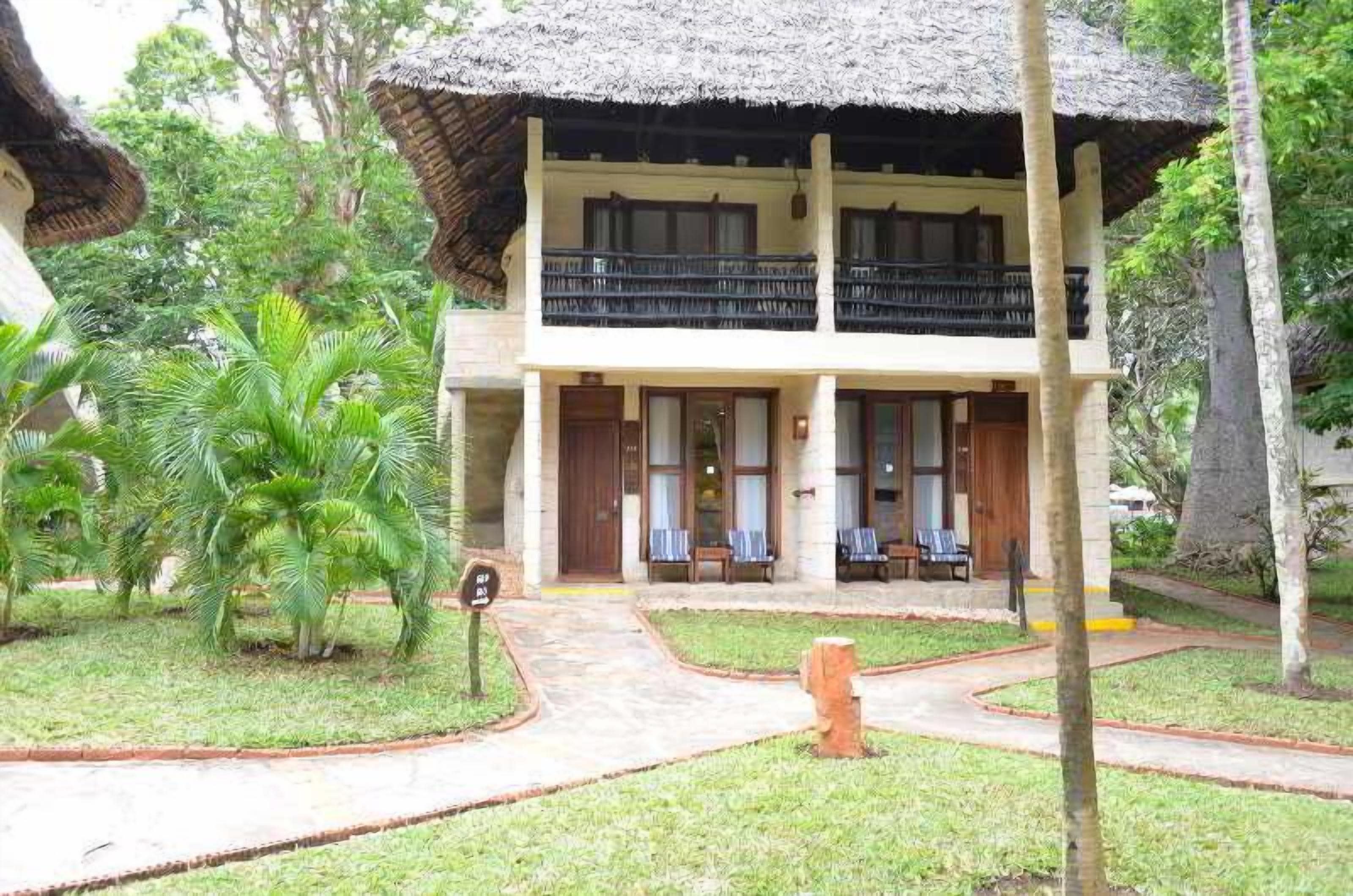 A two-story building with a thatched roof, a balcony, and a small garden area with palm trees.