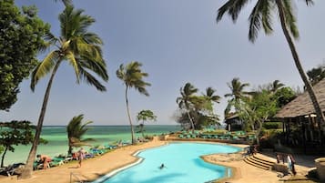 Zona de piscina con vistas despejadas al océano, rodeada de palmeras y sillones de descanso.