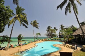 A pool area with a clear view of the ocean, surrounded by palm trees and lounge chairs. - Baobab Beach Resort (Diani Beach)