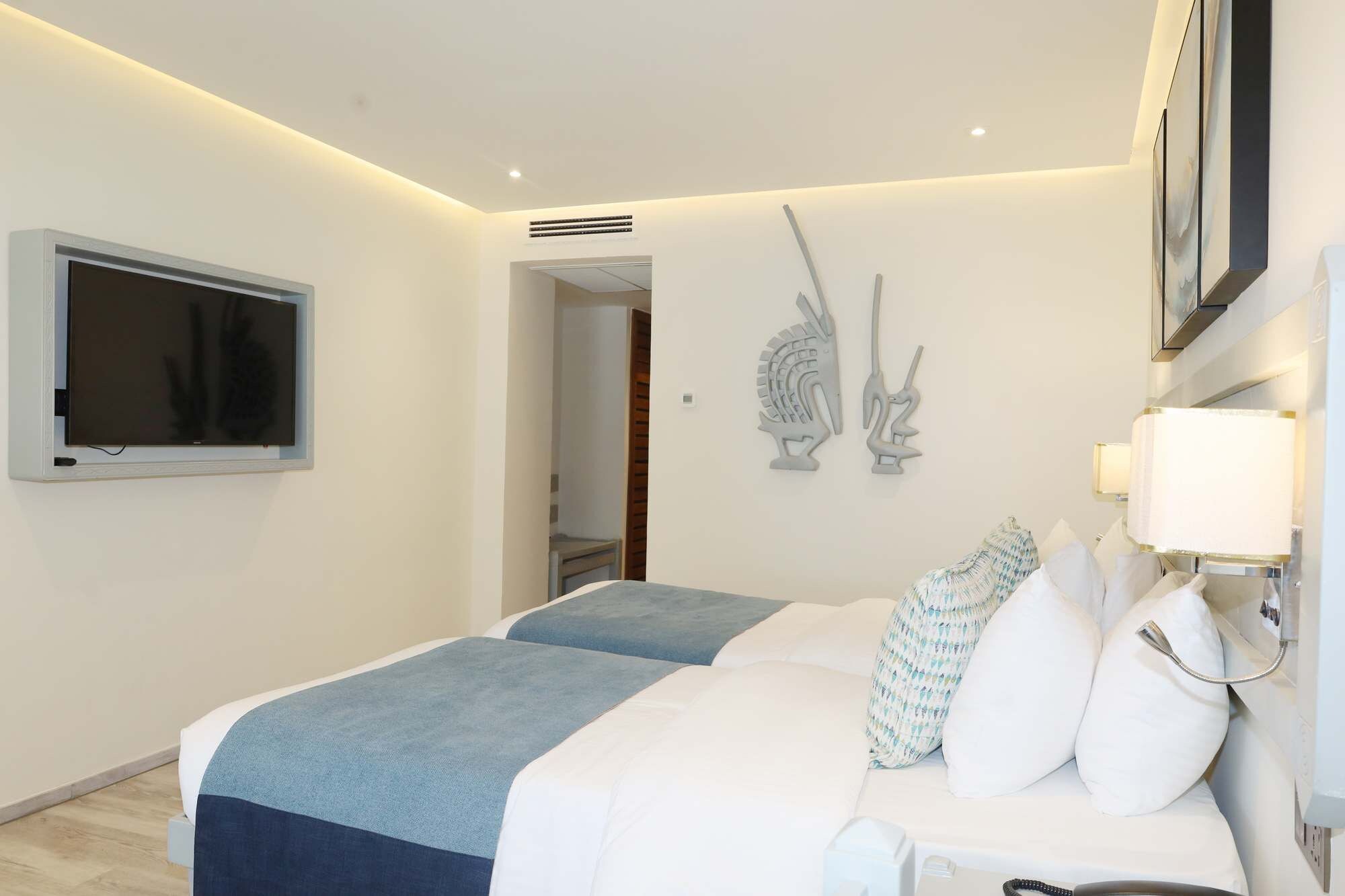 A hotel room with a bed, a TV, a wall-mounted lamp, and decorative wall art.