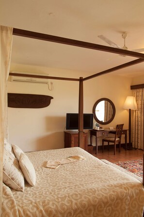 A bedroom with a four-poster bed, a desk with a chair, a television, and a mirror. - Baobab Beach Resort (Diani Beach)
