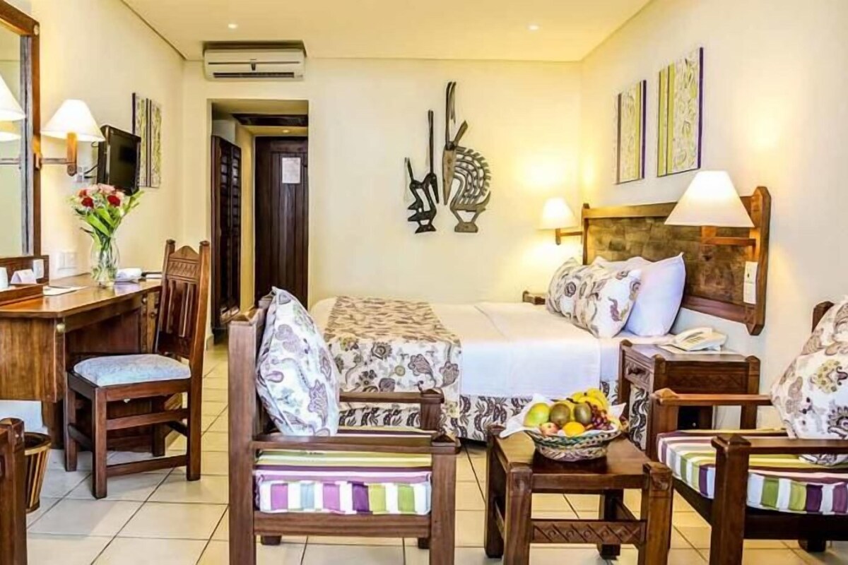 A hotel room with a bed, two bedside tables, a desk with a chair, a small table with a chair, and a mirror.