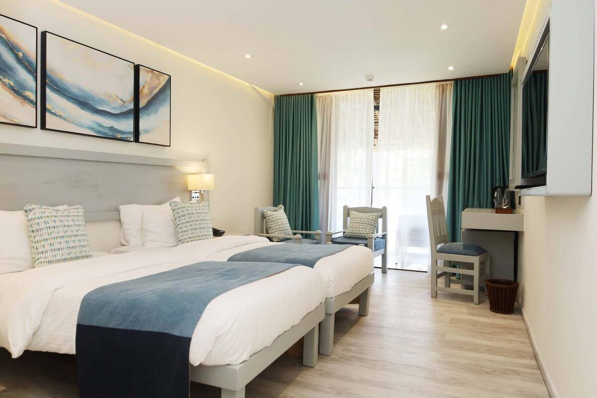 A hotel room with two beds, a desk, a chair, and a TV.