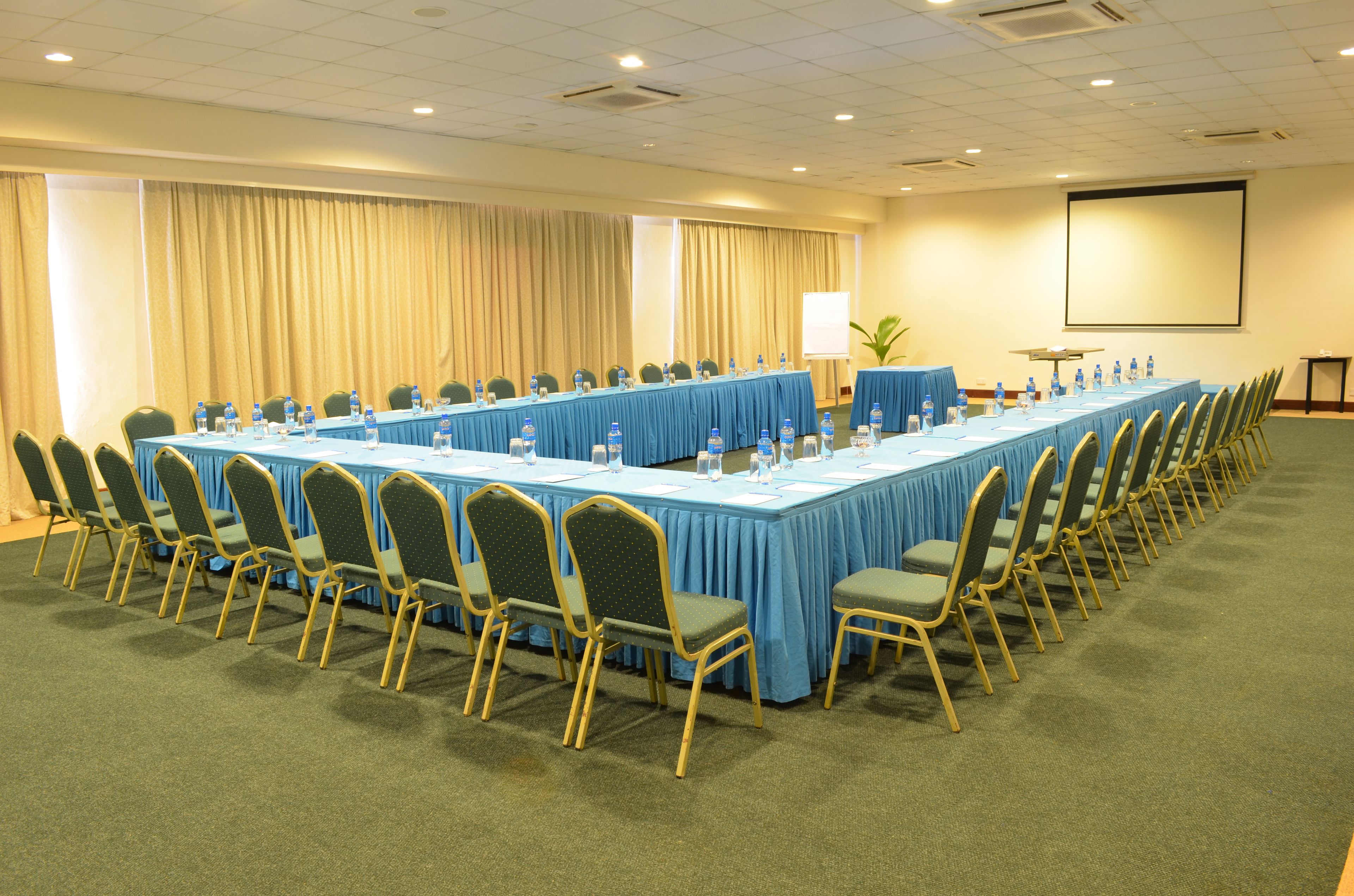 A conference room with a long table, chairs, water bottles, and a projector screen.