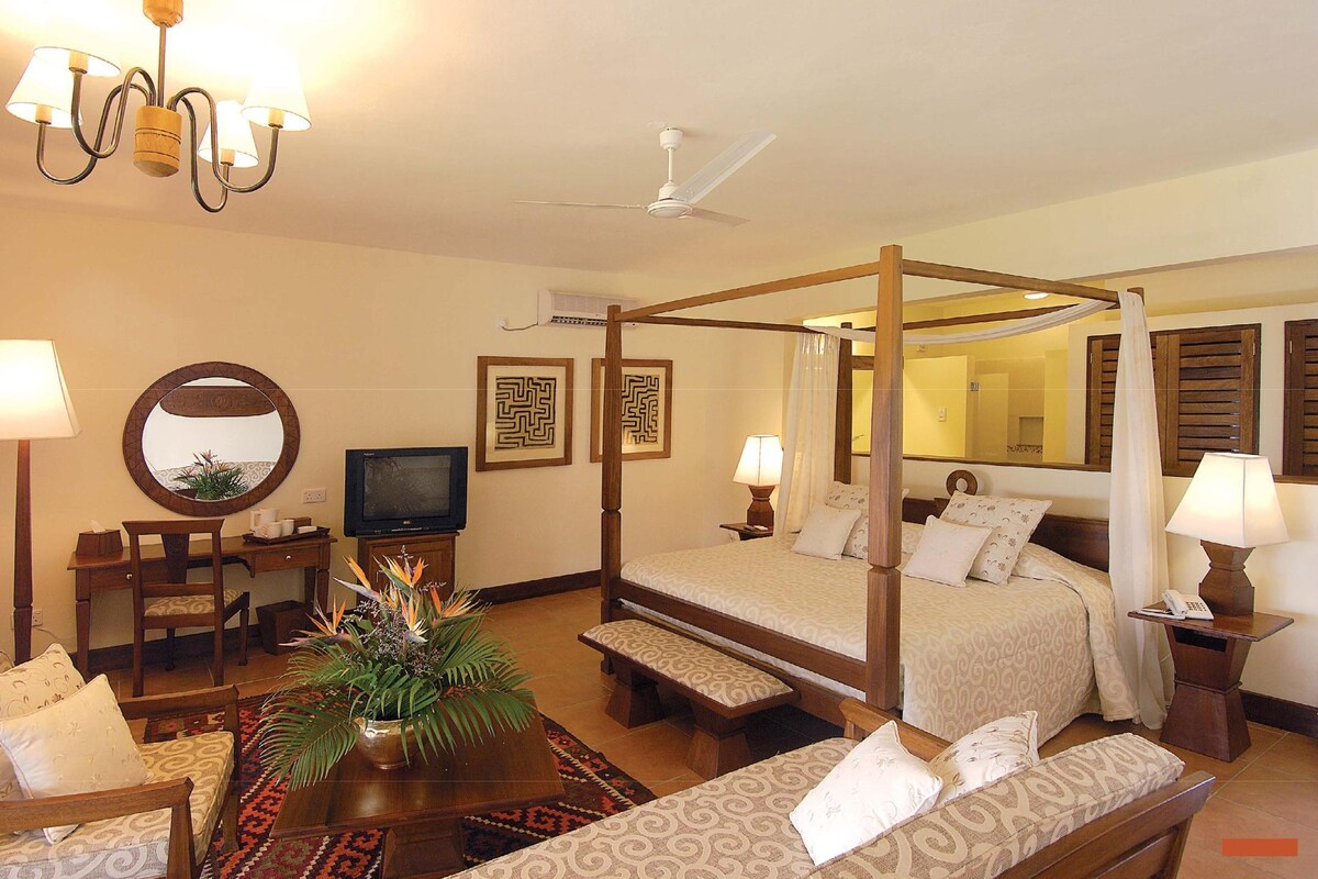A four-poster bed with a canopy, a desk with a chair, a television, and a mirror on the wall.