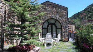 A stone building with a large arched window, surrounded by greenery and outdoor seating. - Bonavida (Canillo)
