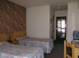 Quarto de hotel com duas camas, cabeceira de madeira, escrivaninha e uma cadeira.