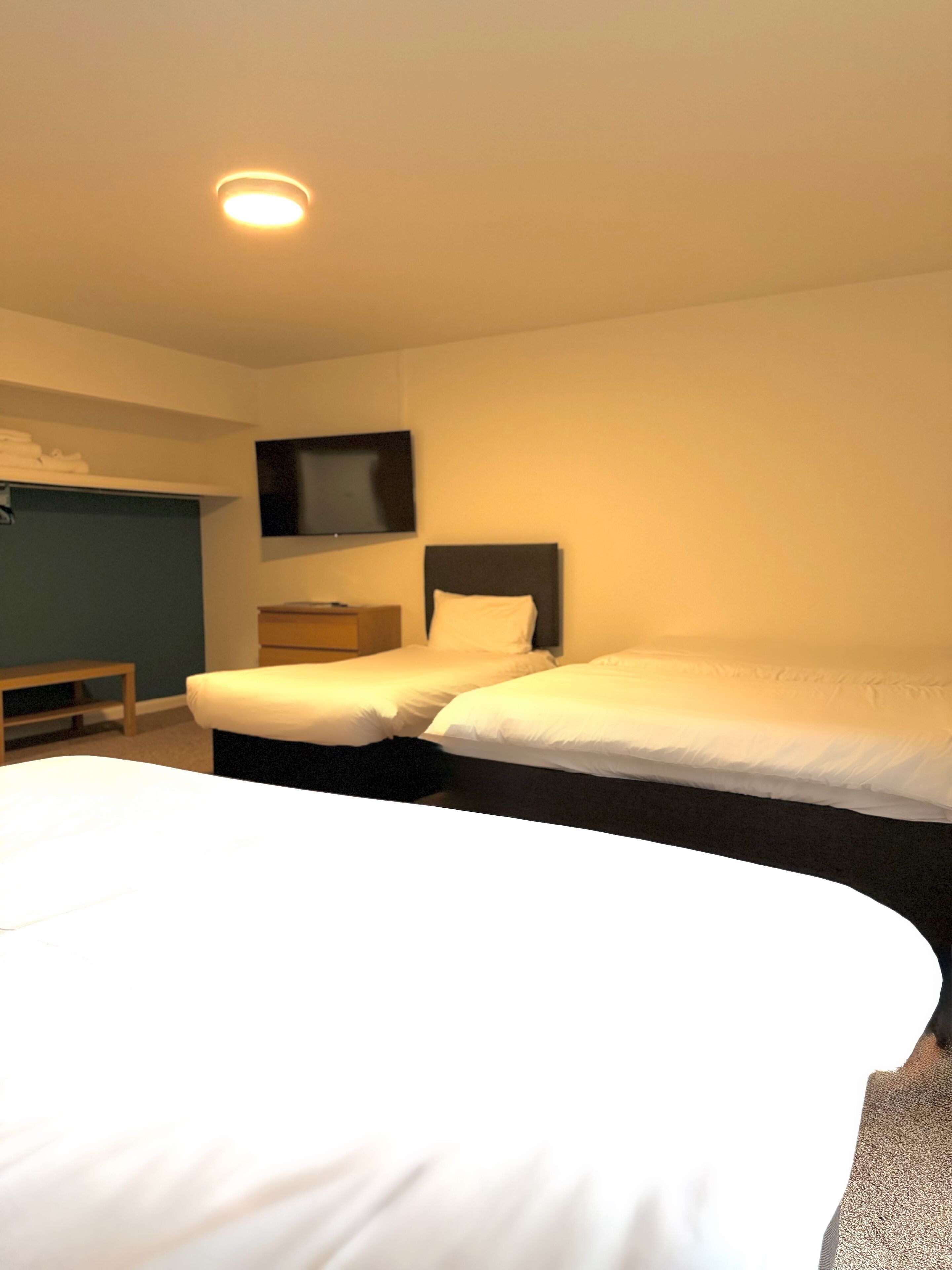 A hotel room with a large bed, two smaller beds, a flat-screen TV, and a desk.