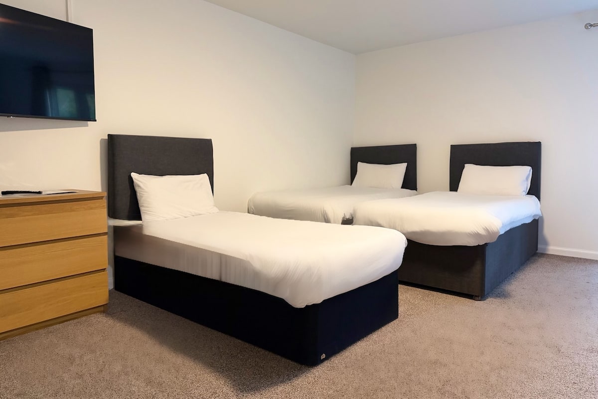Ein Zimmer mit zwei Einzelbetten, einem Holzkleiderschrank und einem an der Wand befestigten Flachbildfernseher.