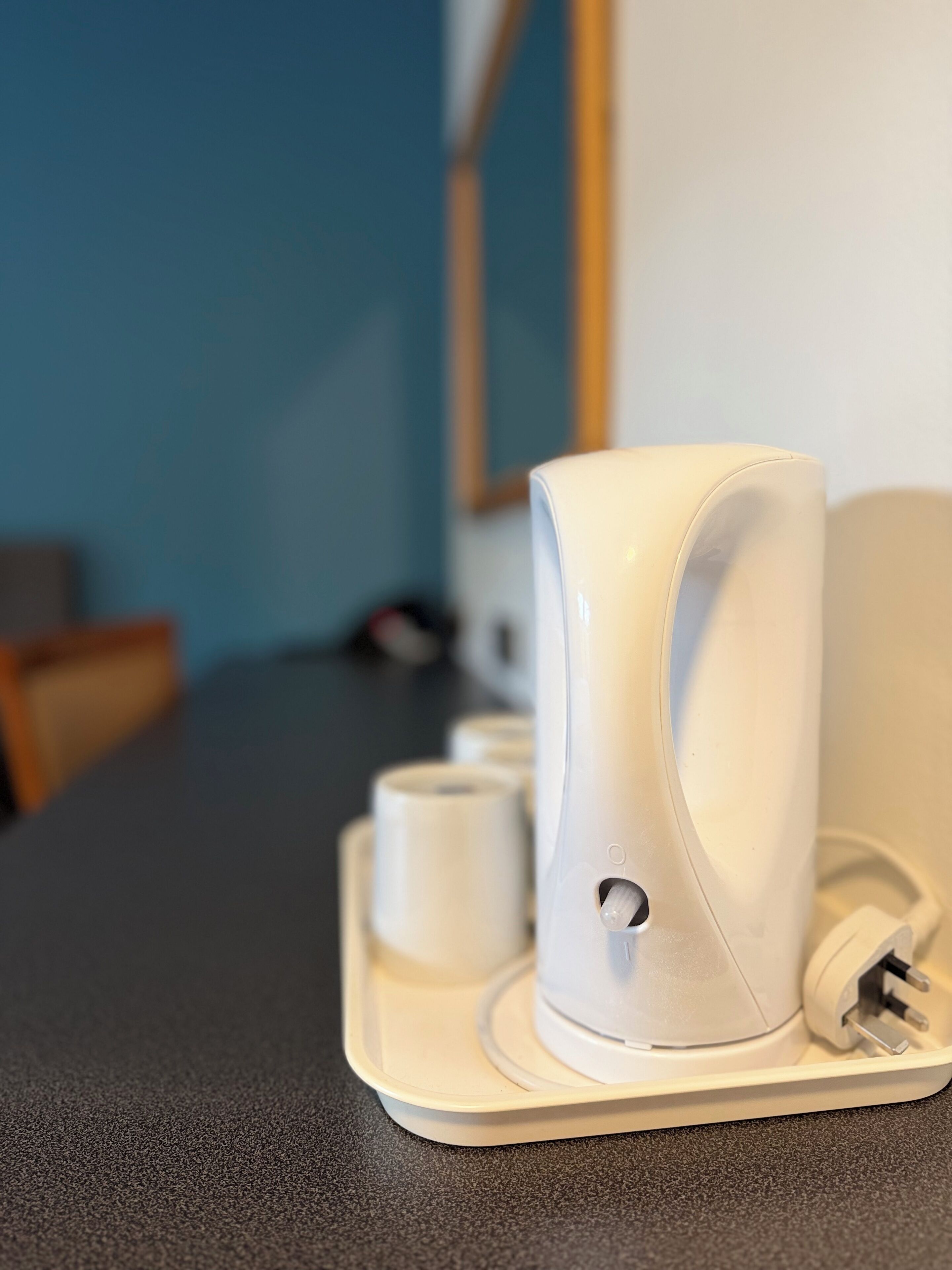 A white, modern coffee machine on a countertop with a power cord plugged in.